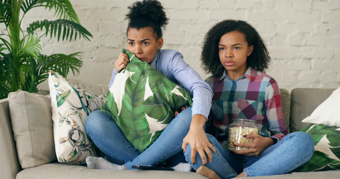 Duas mulheres assistindo séries na televisão com pipoca