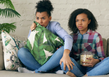 Duas mulheres assistindo séries na televisão com pipoca