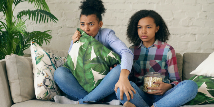Duas mulheres assistindo séries na televisão com pipoca